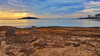 Coastal sunset over rocky shoreline with distant port cranes and bicycles