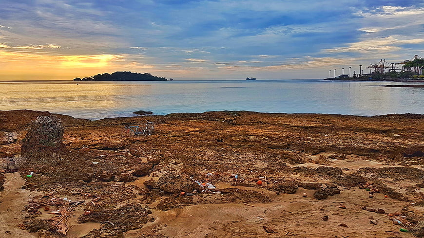 Coastal sunset over rocky shoreline with distant port cranes and bicycles