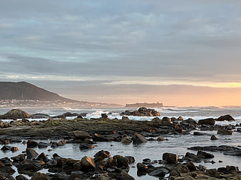 Rocky Coastline at Sunset with Distant Island and Ocean Waves