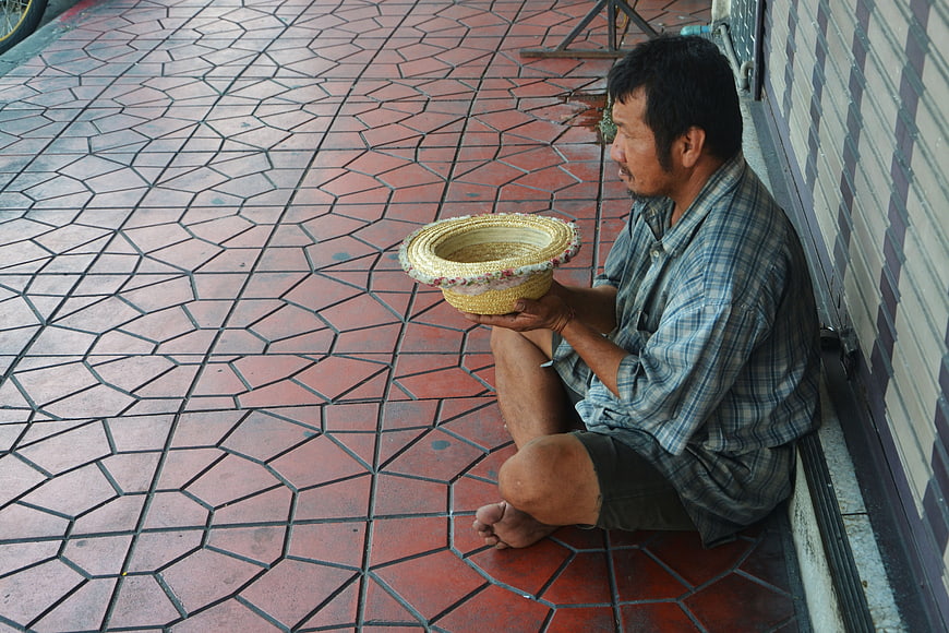 Man sitting on sidewalk holding woven begging bowl