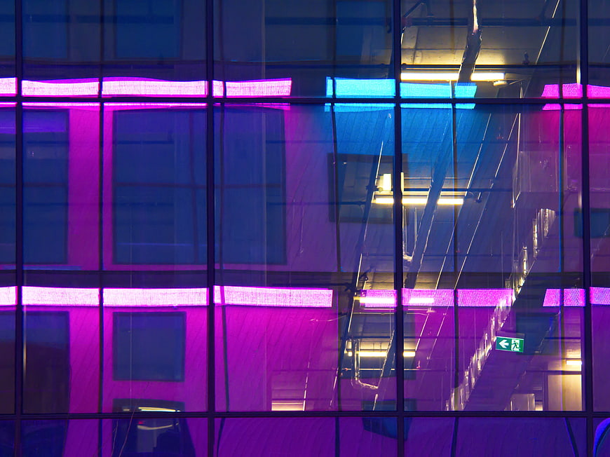Abstract purple and blue neon lights reflecting on modern glass building facade