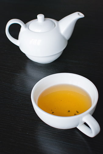White teapot and cup of tea on dark wood table