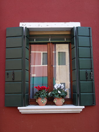 Red wall window with green shutters and potted flowers