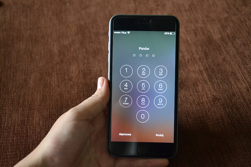 Hand holding smartphone displaying keypad interface on brown textured background
