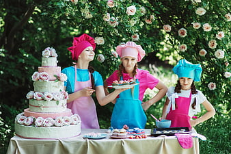Three young girls in chef hats baking outdoors with cake