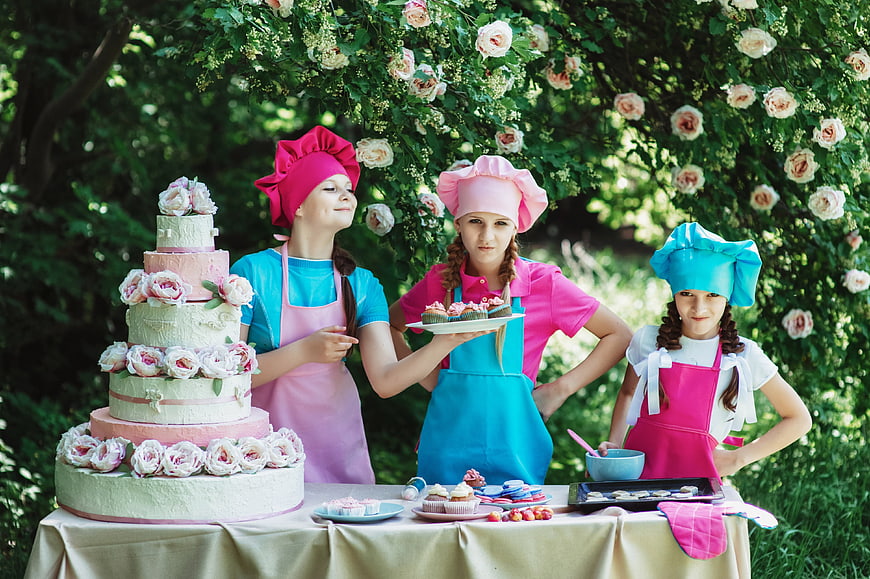 Three young girls in chef hats baking outdoors with cake