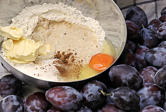Baking ingredients in metal bowl with fresh dark plums