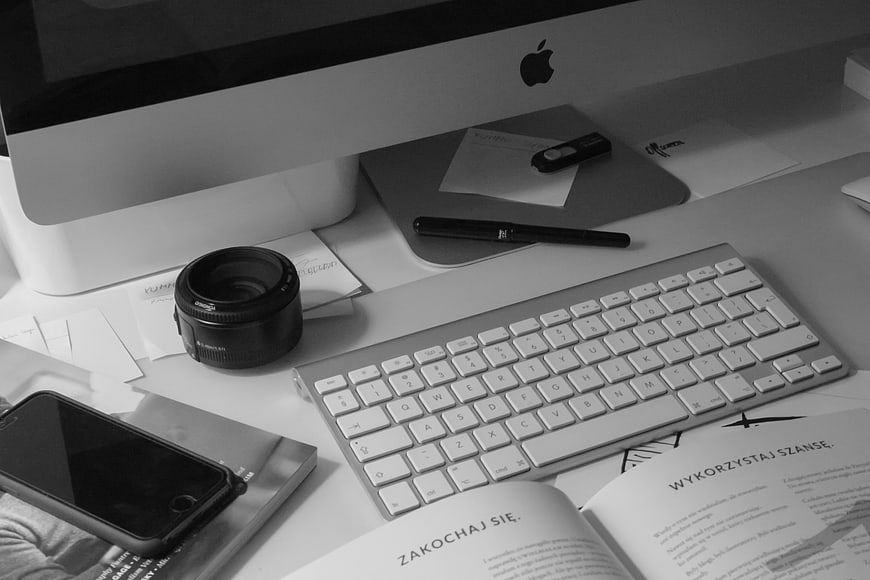 Black and white workspace with iMac, keyboard, and camera lens