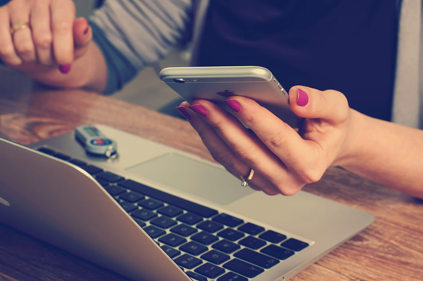 Woman using smartphone with laptop and USB drive on desk