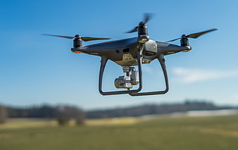 Professional camera drone flying over a green field against a blue sky