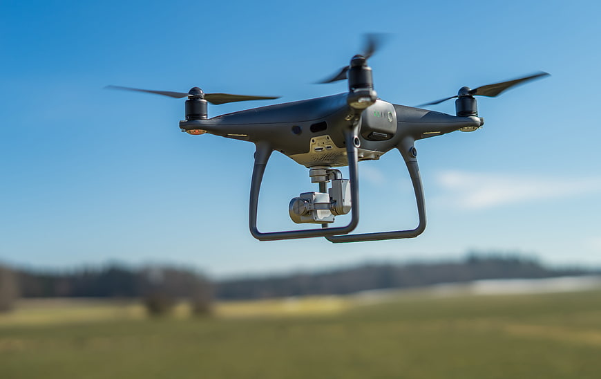 Professional camera drone flying over a green field against a blue sky