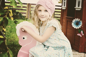 Cute blonde girl in pink hat on rocking horse