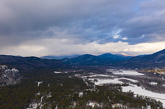Aerial view of snowy mountain valley with frozen lake and clouds
