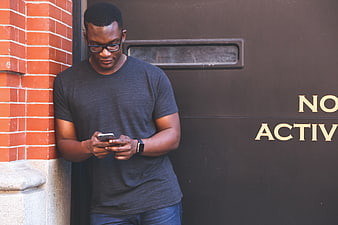 Man Typing on Smartphone Against Brick Wall