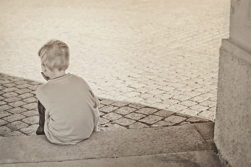 Lonely boy sitting on stone steps in sepia tone