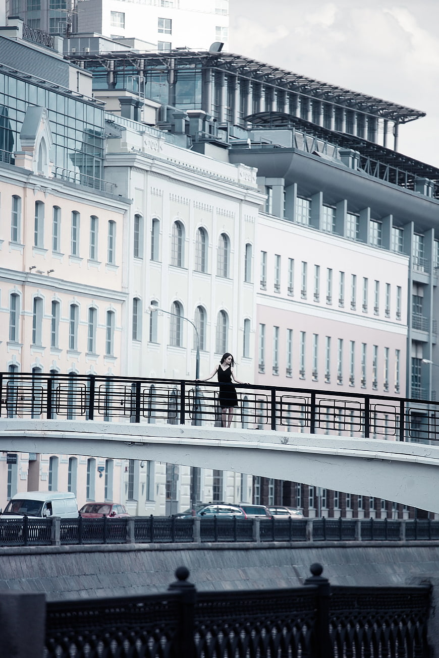 Woman in Black Dress Standing on Urban Bridge