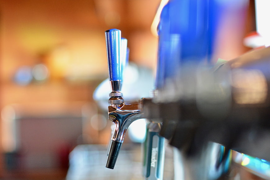 Close-up of beer tap handle with blue top and blurred bar background