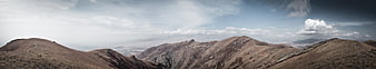 Panoramic view of rugged brown mountain ridges under cloudy sky