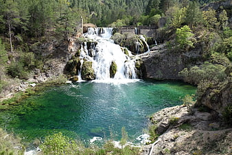 Turquoise waterfall cascading into a clear pool surrounded by forest