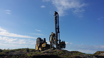 Yellow drilling rig on rocky terrain under blue sky