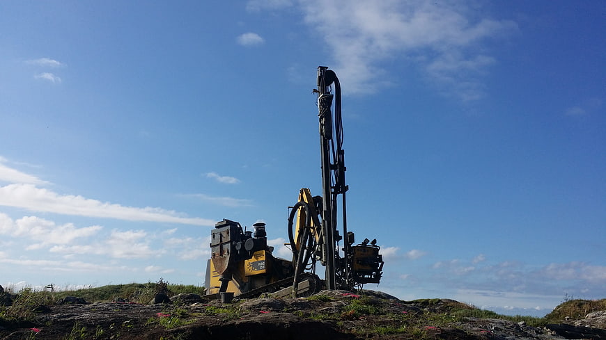 Yellow drilling rig on rocky terrain under blue sky
