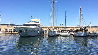 Luxury yacht and sailboats docked in a sunny Mediterranean harbor