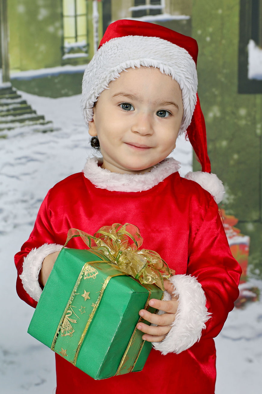 Cute toddler girl in Santa suit holding Christmas gift