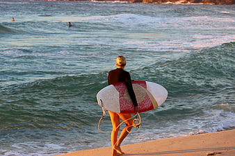 Female Surfer Walking on Beach with Surfboard at Sunset