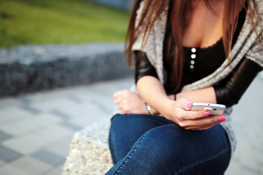 Woman Using Smartphone Outdoors on Stone Bench