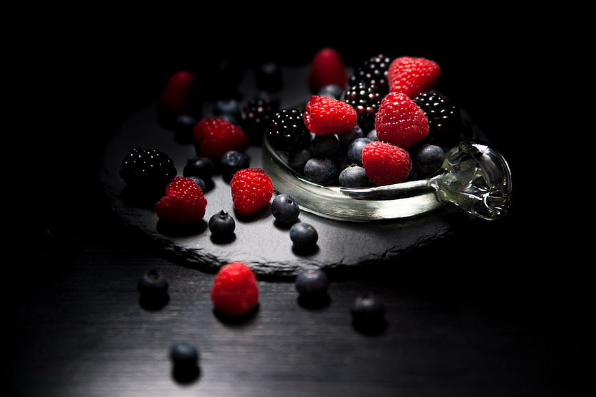 Dark moody mixed berries in glass bowl on slate