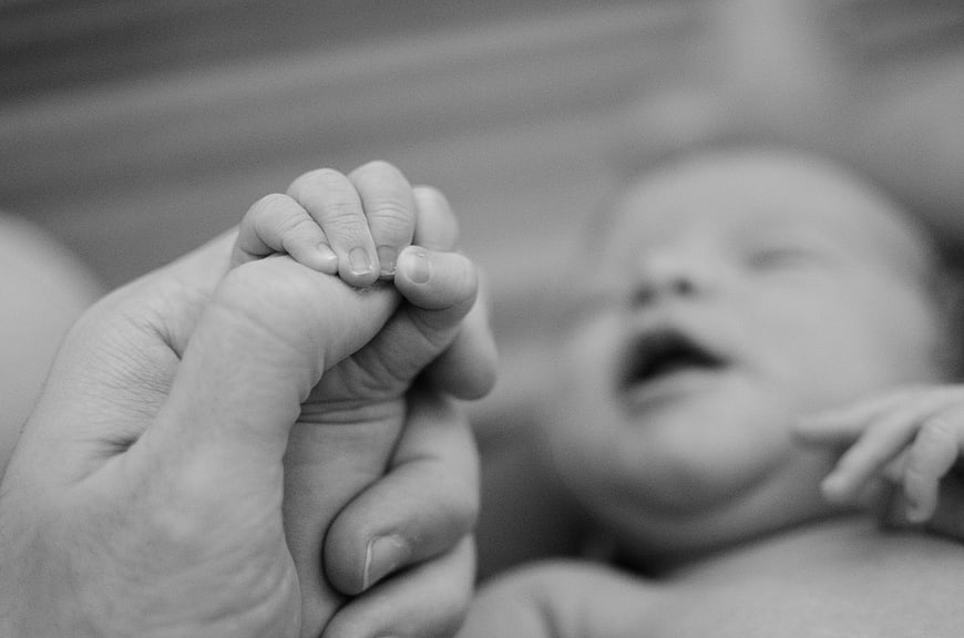 Black and white photo of baby holding adult finger