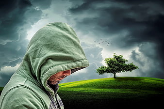 Man in Hoodie Looking at Tree on Hill Under Stormy Sky