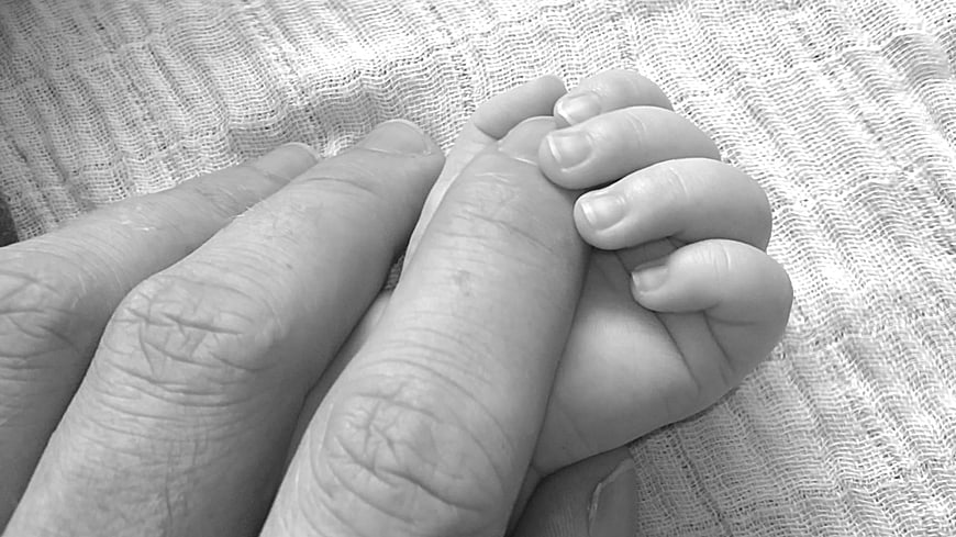 Black and white close-up of adult and baby hands holding