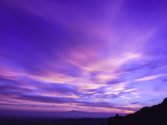 Vibrant purple and pink sunset sky over mountain silhouette