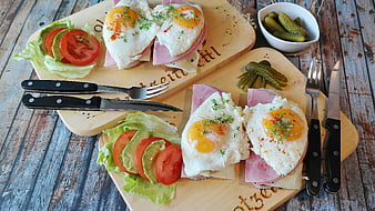 Hearty breakfast with fried eggs, ham, and fresh salad on wooden boards