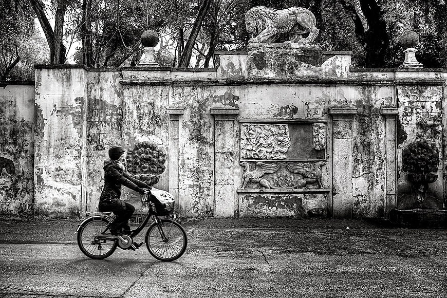 Woman Riding Bicycle Past Ornate Greyscale Wall