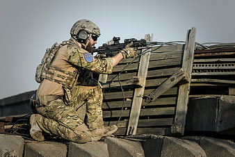 Soldier in tactical gear aiming rifle from cover