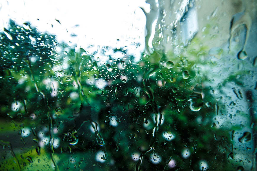Raindrops on Window Glass with Blurred Green Trees Background