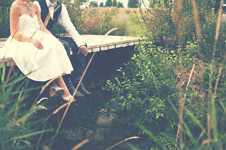 Bride and Groom Sitting on Wooden Bridge in Nature