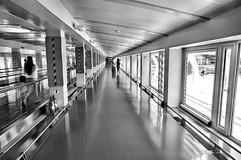 Black and white photo of a woman running with luggage in a modern airport corridor