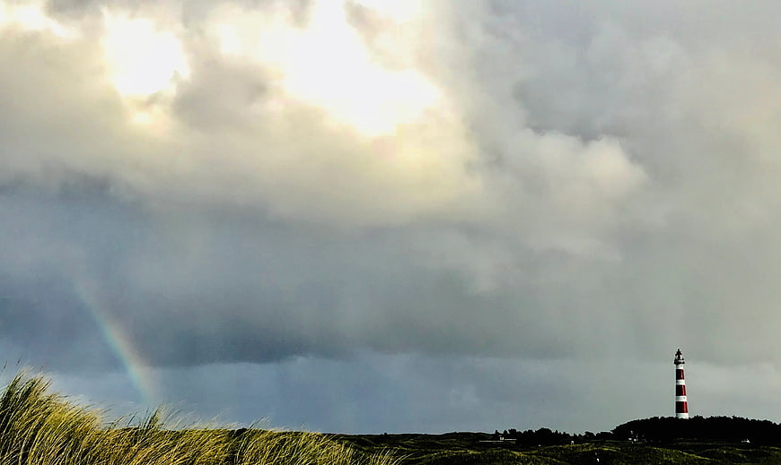 Lighthouse on Dunes with Rainbow and Dramatic Clouds