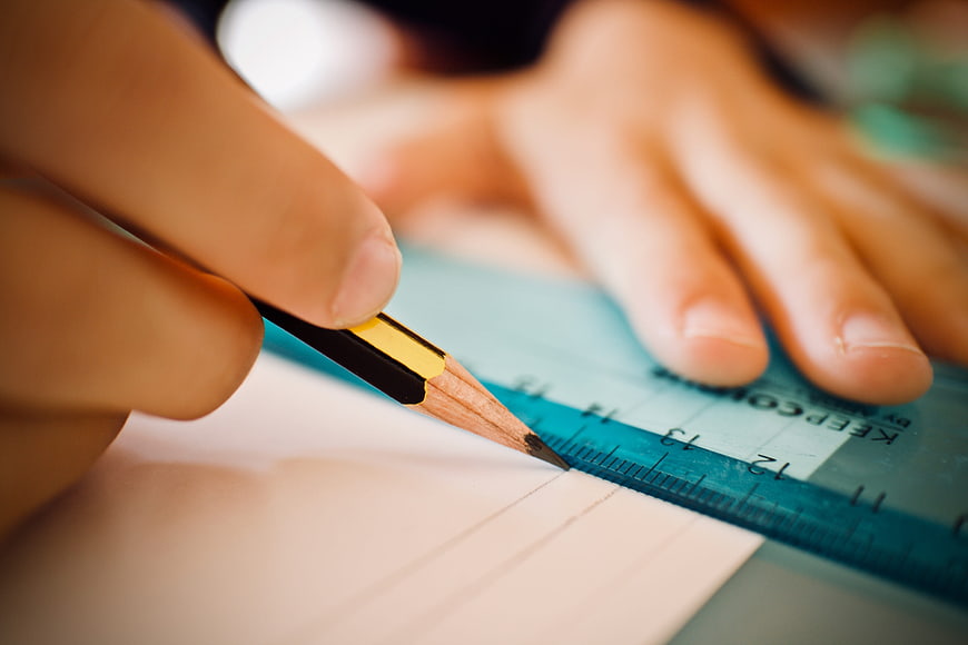 Close-up of hands drawing straight lines with pencil and ruler