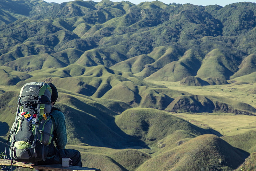 Hiker with Backpack Sitting on Bench Overlooking Rolling Green Hills