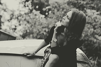 Contemplative woman sitting on vintage car hood in black and white