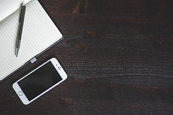 Flat lay of smartphone, notebook, and pen on dark wood