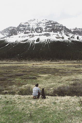 Man and Dog Sitting in Mountain Meadow Landscape