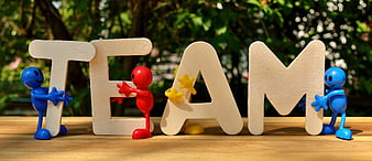 Colorful toy figures holding wooden TEAM letters on table