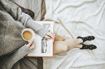 Woman reading book and drinking coffee in bed