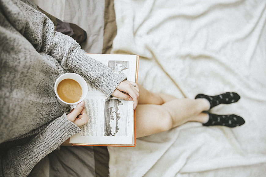 Woman reading book and drinking coffee in bed