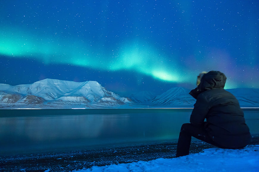 Person Watching Aurora Borealis Over Snowy Mountains